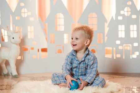 可爱的金发小男孩在睡衣附近的圣诞玩具纸房子