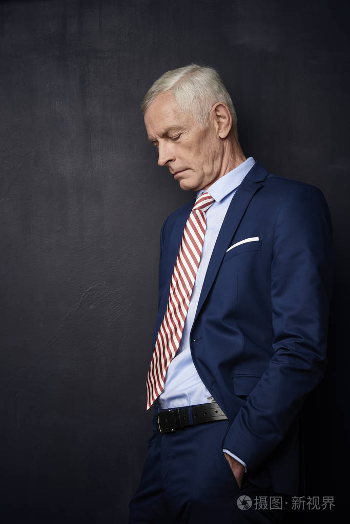 严重成熟商人站在黑墙前的侧面观