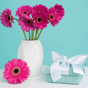 母亲节快乐, 妇女节, 情人节或生日粉彩糖果蓝色背景。深粉红色的 gerberas 在一个花瓶的桌子上, 有美丽的礼物