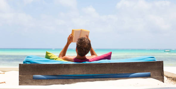 放松的人读的书在豪华躺椅享受夏天假期在美丽的海滩