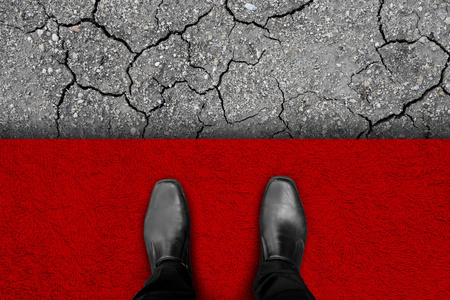 黑鞋站在红地毯地板上, 贫富之间的边缘。在他面前是干土代表穷人