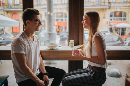 快乐的年轻情侣在酒吧或餐馆里约会很愉快。他们讲自己的故事, 喝茶或咖啡, 吃沙拉和汤