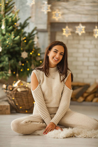 年轻的女人微笑着坐在圣诞树的背景上