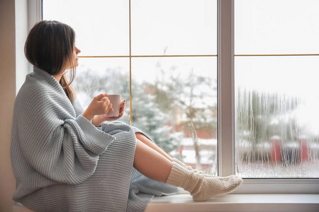 冬日的窗户边喝茶边放松的年轻女子