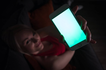一个女人在晚上躺在沙发上, 拿着一部手机