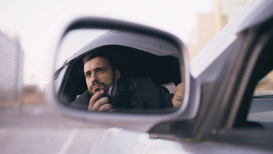 坐在车里面，单反相机拍摄的年轻私家侦探人的一面镜子里