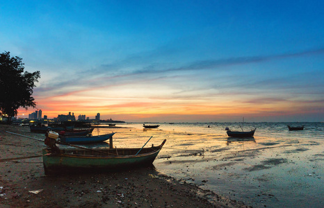 在泰国芭堤雅夕阳黄昏的海滩上停泊着老渔船的热带海滩景观