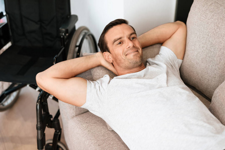 残疾人躺在沙发上休息, 双手放在头后。附近是他的轮椅
