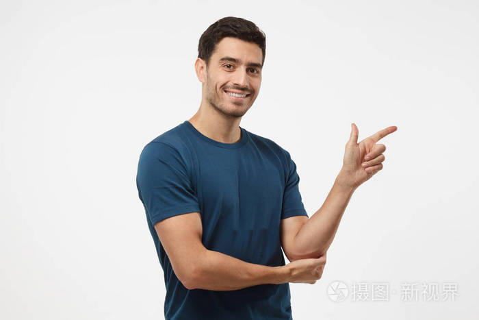有吸引力的年轻男子在蓝色的 t-shirt 指向右与他的手指在灰色背景上