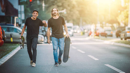 两个临滑板车手走在街上举行 skatebo