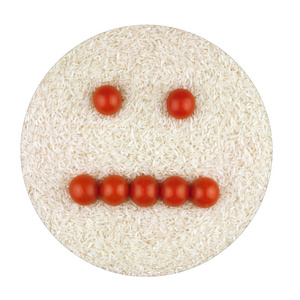不愉快的笑脸由红西红柿在大米的背景