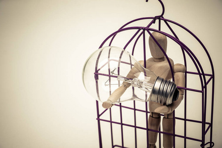 模特人物手持白炽灯泡的笼子里的木头人物模特照片