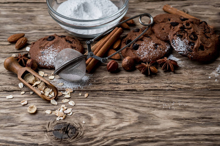 巧克力曲奇饼与糖粉在碗和用具在木背景与拷贝空间