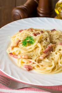 经典的面食 carbonara。意大利面配培根，鸡蛋蛋黄和帕尔玛奶酪在白板上深色木制背景