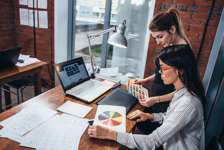年轻女性在新的网页设计使用颜色色板和剪影坐在书桌在现代办公室