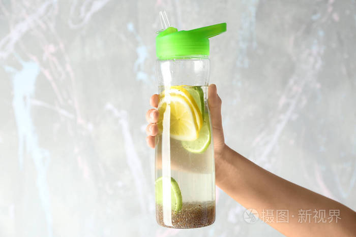 手拿着瓶水和籽和柠檬在明亮的背景上