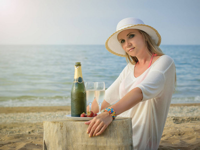 在她的胳膊上有五彩手镯的妇女与一瓶香槟在海边