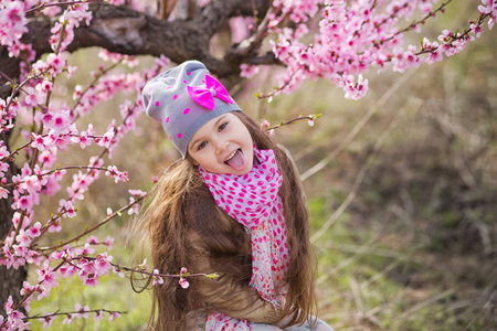可爱的漂亮时髦的金发女郎站在春天的田野上, 一棵粉红色的花. 微笑的女孩穿着粉红色的春天季节