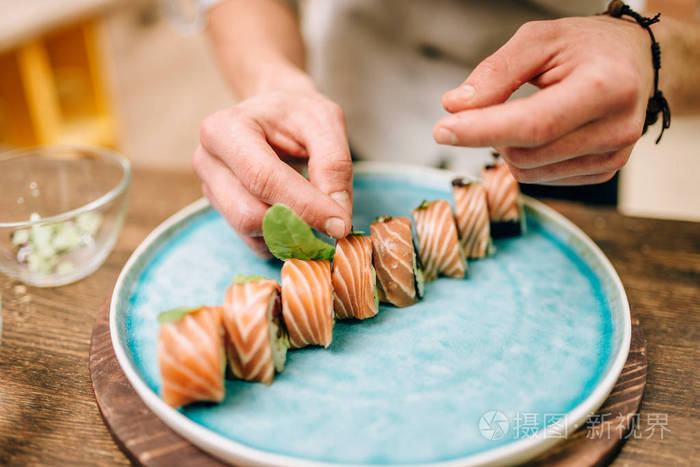 男厨师在蓝色盘子上装饰寿司卷传统日本料理海鲜