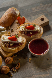 关闭碗与果酱和美味的三明治与草莓, 坚果和奶酪在木板上, 顶部视图