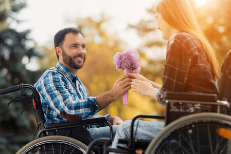 一对夫妇在轮椅上的残疾人在公园相遇。一个男人给一个女人一束鲜花