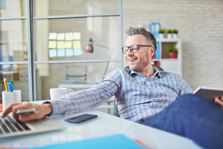 乐观的人乐观的 middleaged 商人享受轻松的工作与现代设备, 他打字在