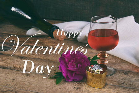一杯红酒, 瓶子和玫瑰在乡间的木桌上。情人节还活着。概念贺卡与题词快乐情人节。文本的复制空间