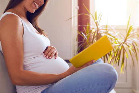 微笑着怀孕的女人坐在沙发上，阅读本书