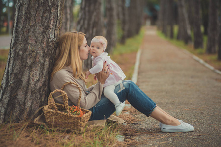 快乐的年轻母亲 sylish 打扮与女婴穿着粉红色的礼服可爱的花一生一起坐在森林附近的树木和篮子与野生浆果