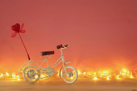 情人节浪漫的背景与白色复古自行车玩具和闪闪发光的红色的心在它的木桌上