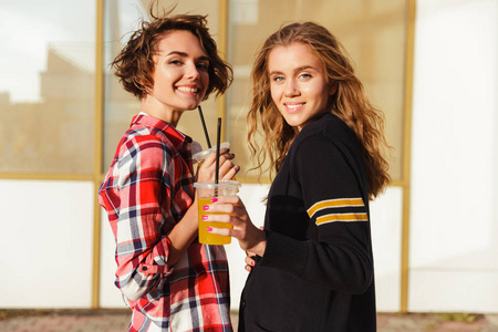 两个微笑的少女戴着墨镜喝橙汁