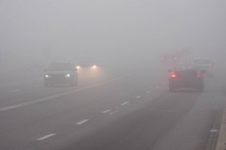 在雾中的汽车。恶劣的冬季天气和危险的汽车交通的道路上。轻型车辆在雾中