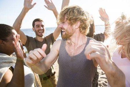 快乐的跨文化的朋友在沙滩上跳舞的时候举起双手