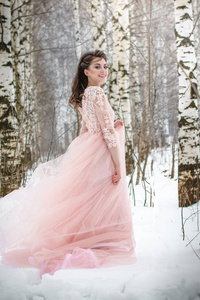 女孩在一个美丽的粉红色连衣裙在冬季森林