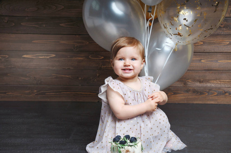 逗人喜爱的可爱的女婴的画像庆祝她的第一个生日与蛋糕和气球