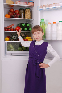 美丽的女孩在冰箱附近与健康食物