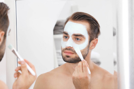 年轻英俊的人在浴室的脸上涂上化妆面具