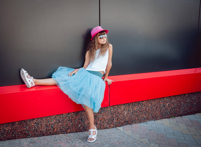 小女孩在粉红色的帽子和花哨的蓝色裙子摆在街上