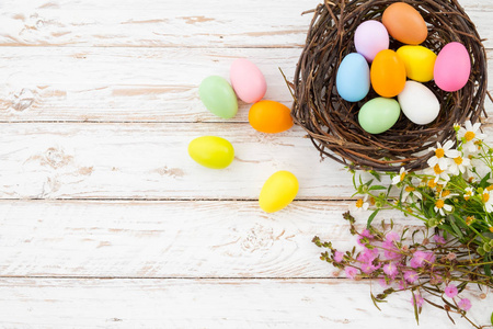 五颜六色的复活节彩蛋在巢与花在质朴的木板背景白色油漆。春节放假。老式的色调风格。顶部视图组合