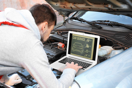 年轻男性技工在修理汽车时使用计算机诊断