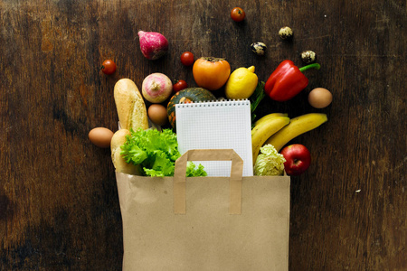 不同保健食品的纸袋和木制背景的笔记本。顶部视图。平躺