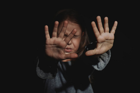 在黑色背景的无助的小女孩.虐待儿童概念照片