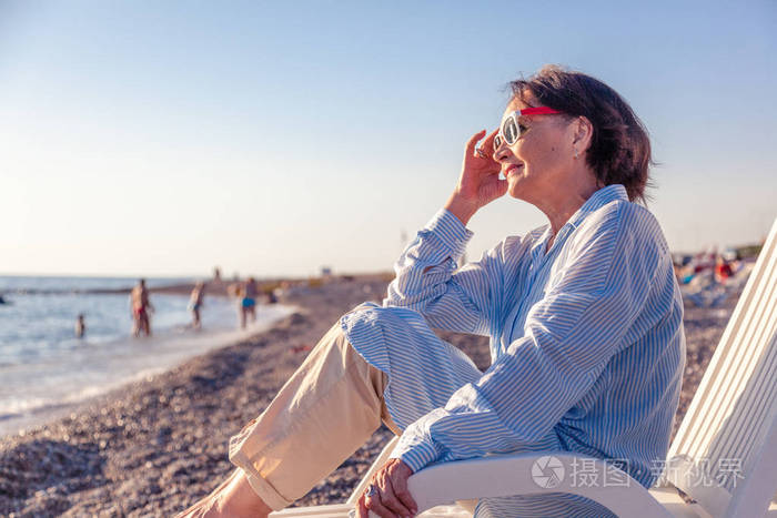 美丽的老太太坐在海滩上的上