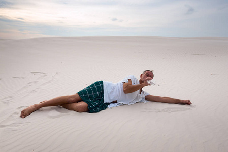 筋疲力尽的人躺在沙子上, 喝着水的残骸