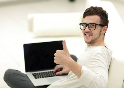 现代年轻的坐在前面的开放式笔记本电脑, 并显示拇指