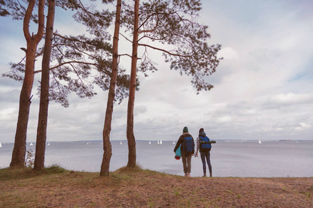 bagpacks 的女朋友独自站在湖边和森林风景的前面。一个探索世界的时髦旅行者