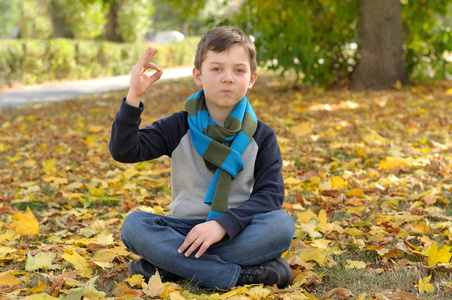 男孩做冥想锻炼坐在黄色秋天叶子照片