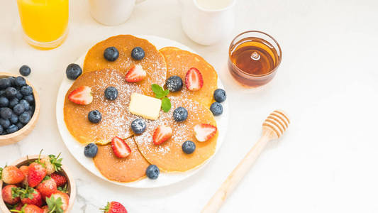 健康早餐配有煎饼蓝莓和草莓水果, 黑咖啡, 牛奶和橙汁在白色的石头桌背景