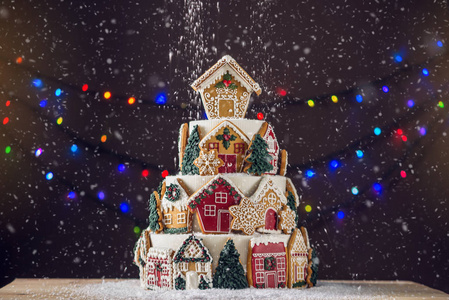 大层次的圣诞蛋糕装饰与姜饼饼干和房子在上面。背景中的树和花环