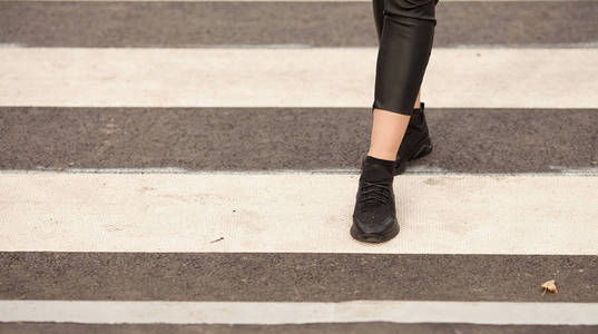 在人行横道上行走的女人腿的闭合。那女人穿着黑色运动鞋